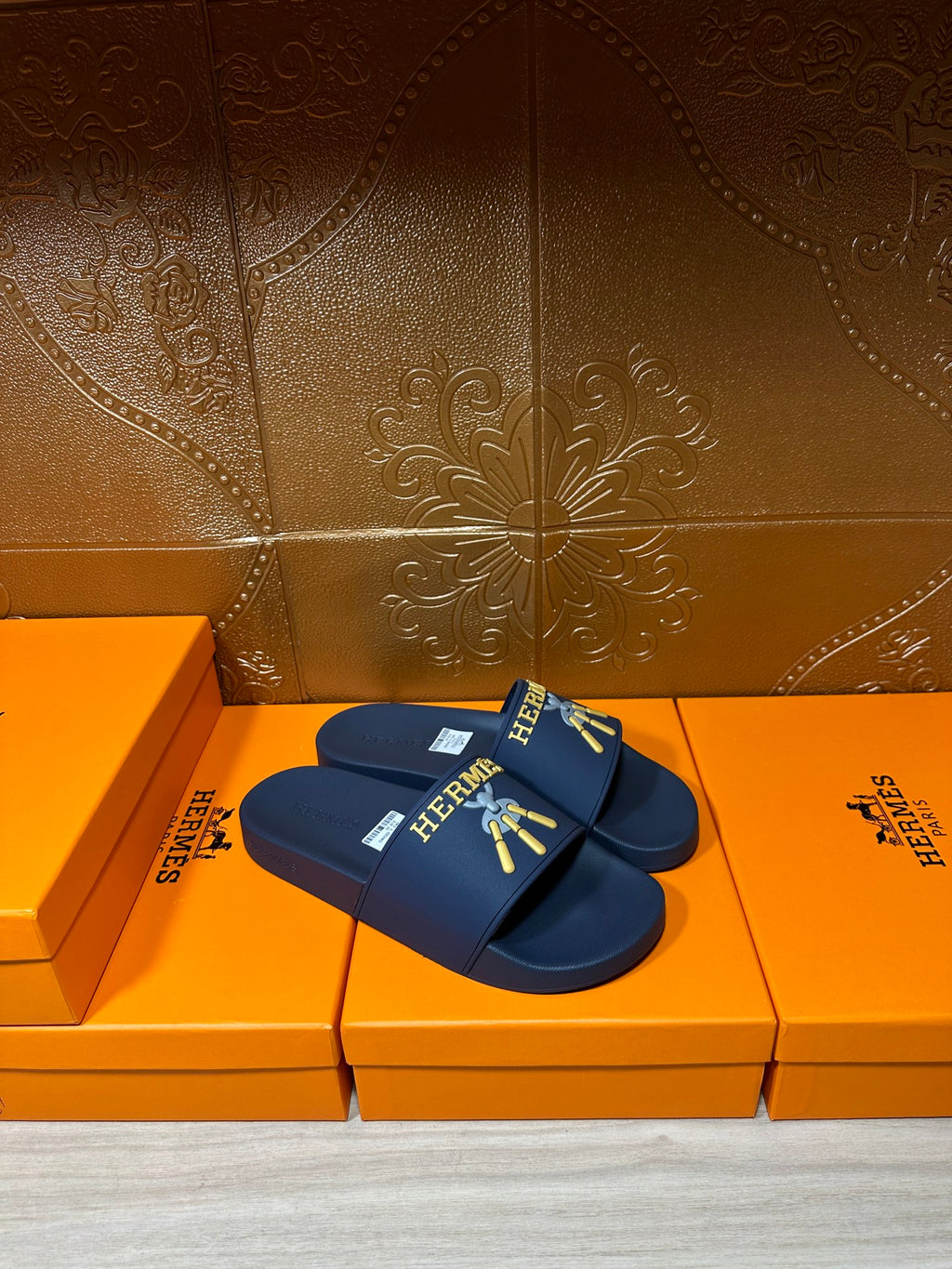 Hermes navy-blue slide sandals with gold HERMES logo and charm graphic