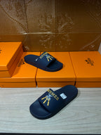 Hermes blue slide sandals, angled view with gold HERMES logo and charm graphic