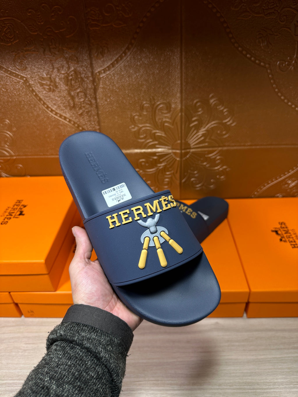 Hermes blue slide sandals held in hand, gold HERMES logo and charm graphic