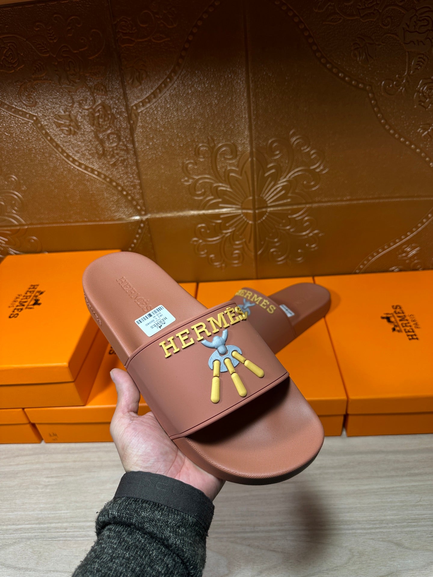 Hermes taupe slide sandal held in hand, multicolor logo patch on strap