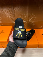 Hand holding a Hermes black slide sandal, showing front logo and white size label.