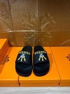 Hermes slide sandals, black leather with gold-and-blue logo detail on the strap.