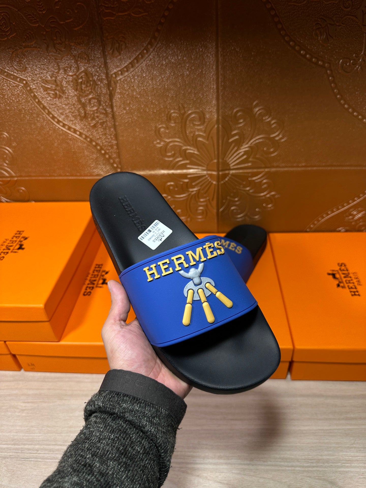 Hermes slide sandals held in hand: blue strap with gold logo on black sole