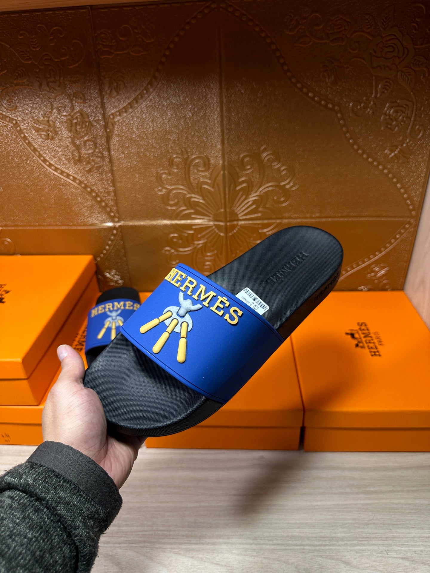 Hermes slide sandals in hand, blue strap with gold logo and black footbed