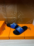 Hermes slide sandals with blue logo strap and black soles, stacked shoe display