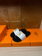 Hermes slide sandals pair with white logo strap, black footbeds, gold emblem detail