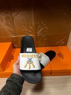 Hermes slide sandal in hand, white logo strap with gold emblem on black