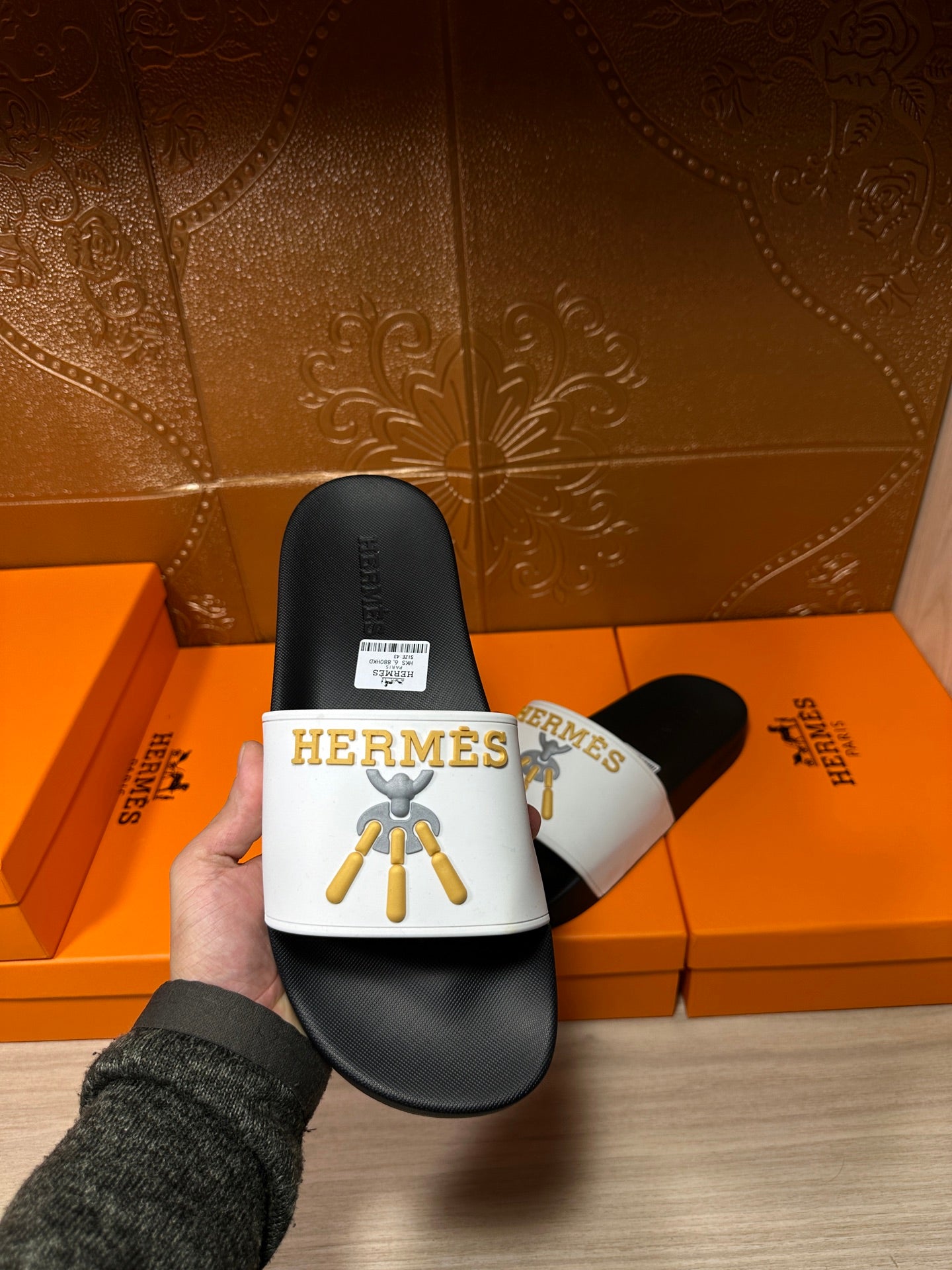 Hermes slide sandal in hand, white logo strap with gold emblem on black