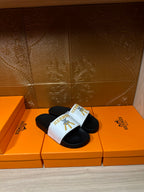 Hermes slide sandals with white strap and gold emblem over black footbed