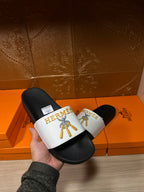 Hermes slide sandal held in hand, black footbed with white logo strap