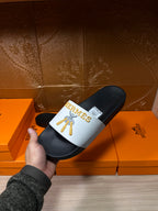 Hermes slide sandal held in hand, white strap with gold emblem, black footbed