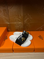 Pair of white slide sandals with black Hermes strap and gold tassel emblem