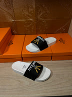 White slide sandal with black Hermes strap and gold tassel motif