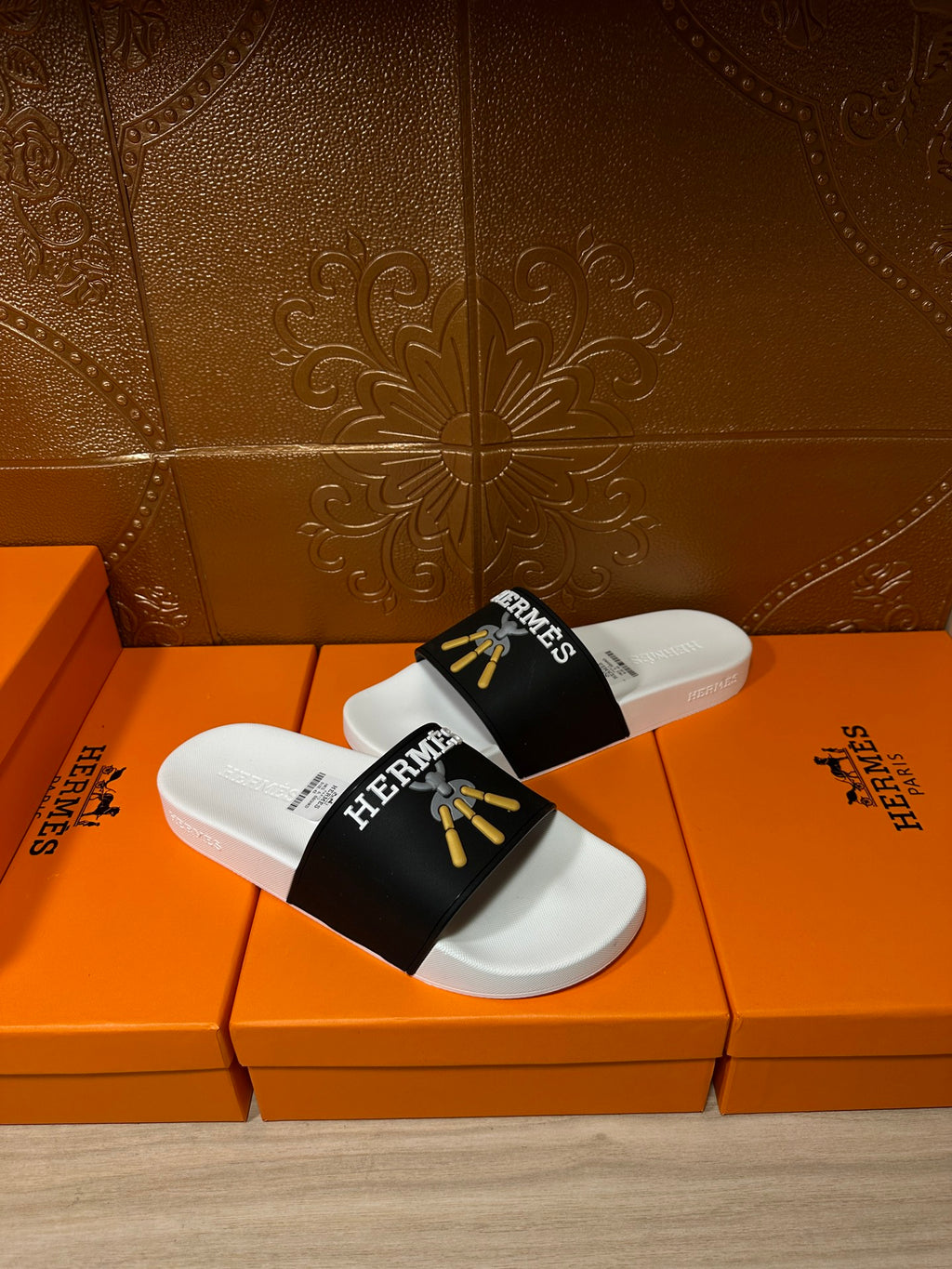 White slide sandals with black Hermes strap and gold tassel graphic