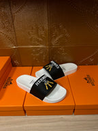 White slide sandals with black Hermes strap and gold tassel graphic