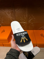 Handheld white slide sandal with black Hermes strap and gold tassel graphic
