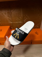 White slide sandal with black Hermes strap and gold tassel graphic, top view