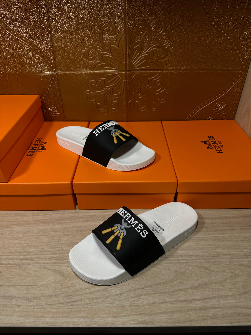 White slide sandals with black Hermes strap and gold tassel detail, side view