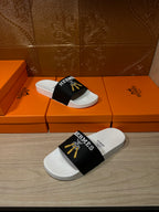 White slide sandals with black Hermes strap and gold tassel detail, side view