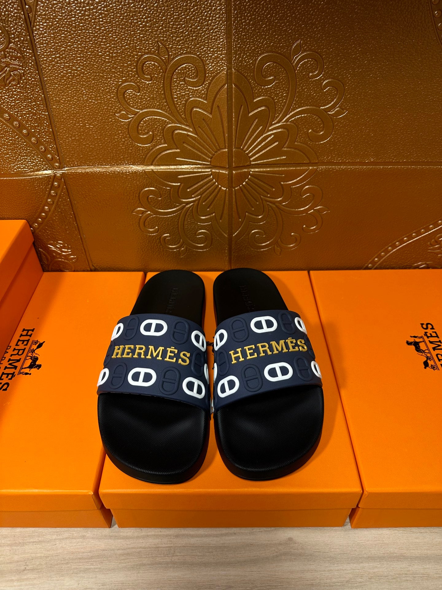 Black slide sandals with navy strap and white H pattern