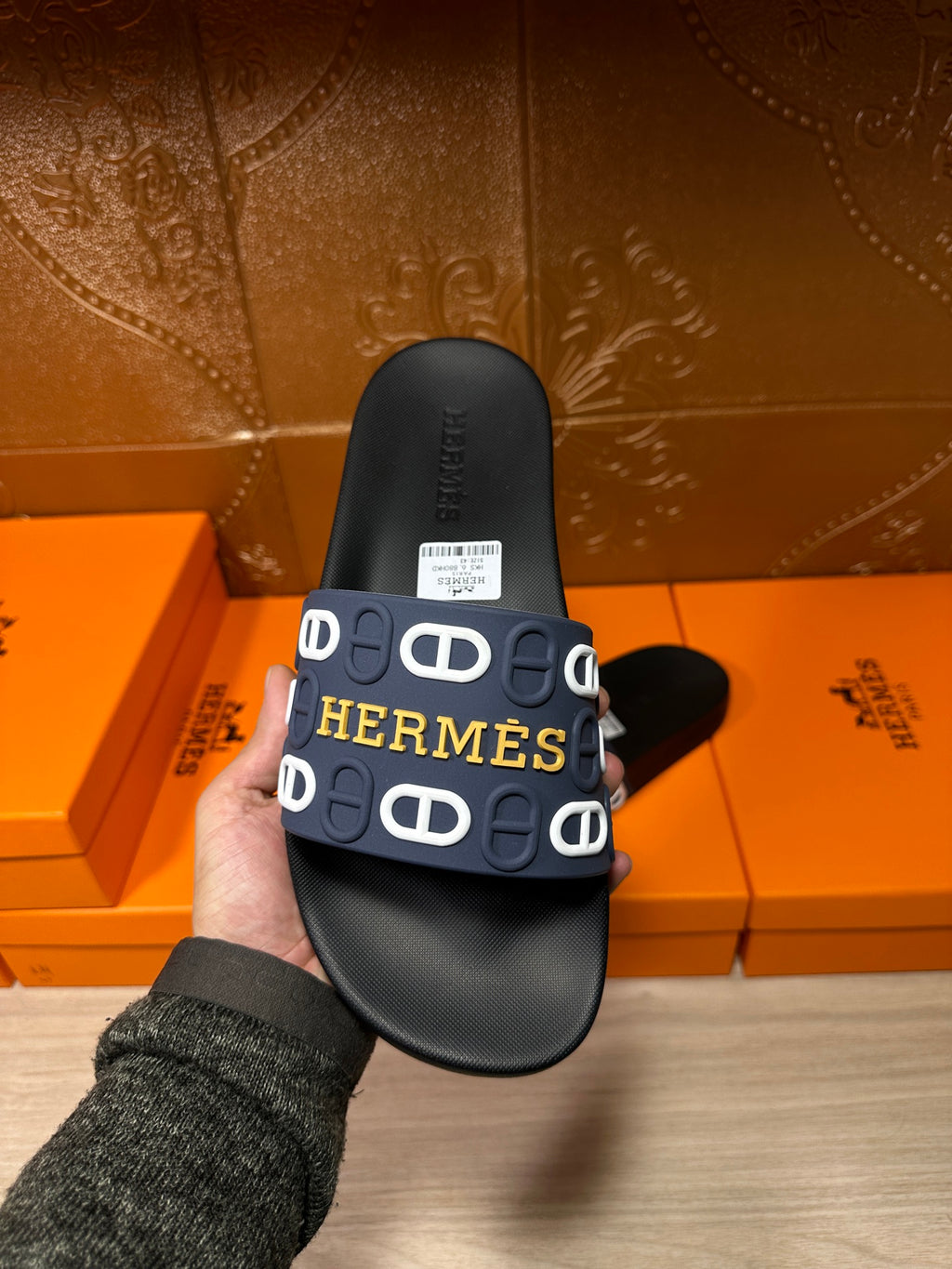 Hermes black slide sandal held in hand, navy strap with white H logo