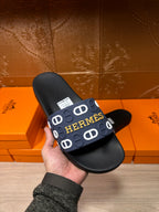 Hermes black slide sandal held up, navy strap with white H logo pattern