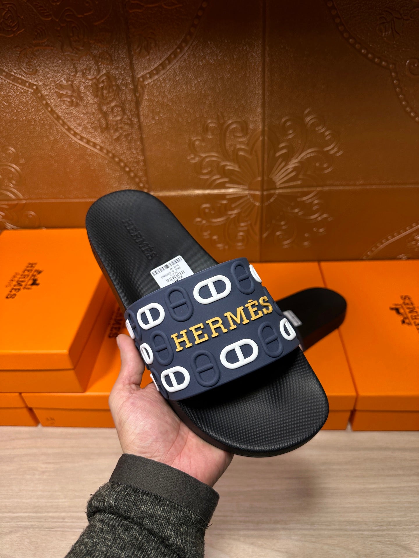 Hermes black slide sandal held up, navy strap with white H logo pattern