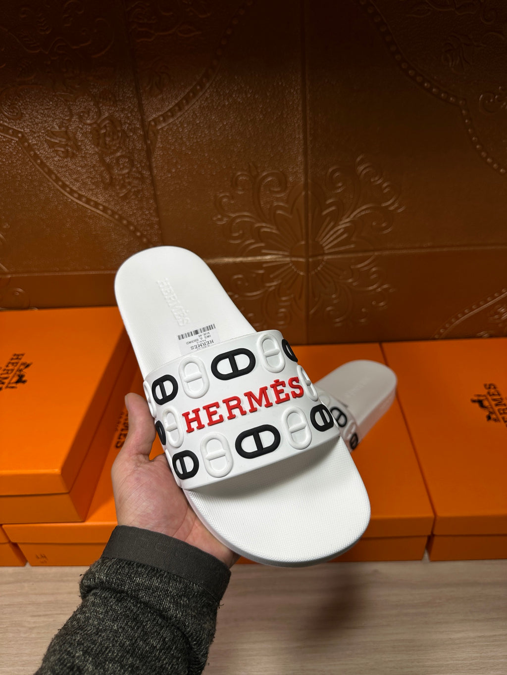 Hermes white slide sandals held in hand, showing the wide logo-printed strap