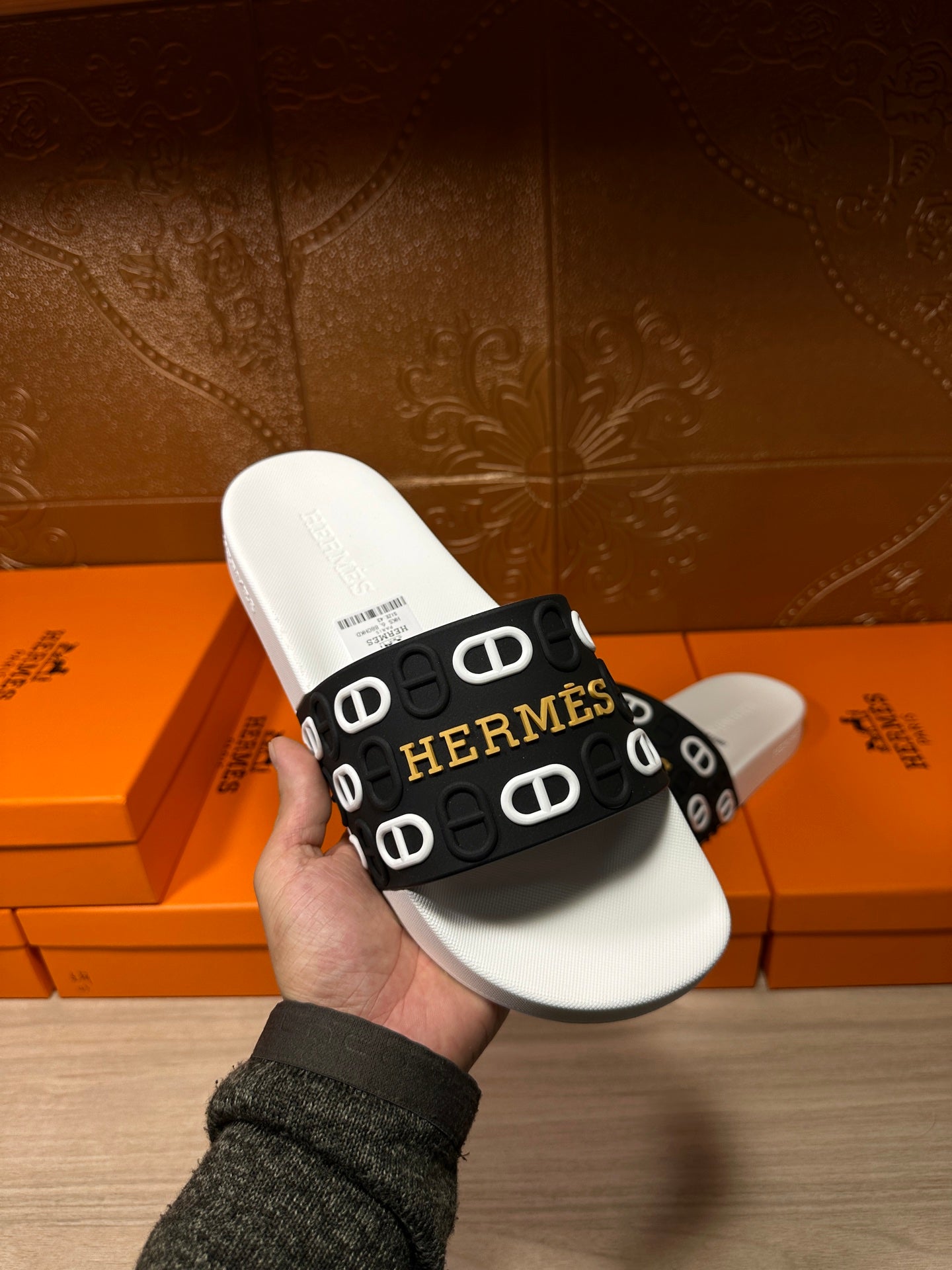 Hermès slide sandal held in hand: black logo strap on white footbed.