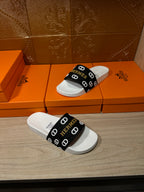 Hermès sandals with black logo band and white footbed, angled view.