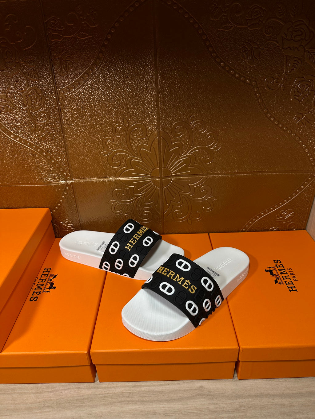 Hermès slide sandals with black logo strap over white footbeds.