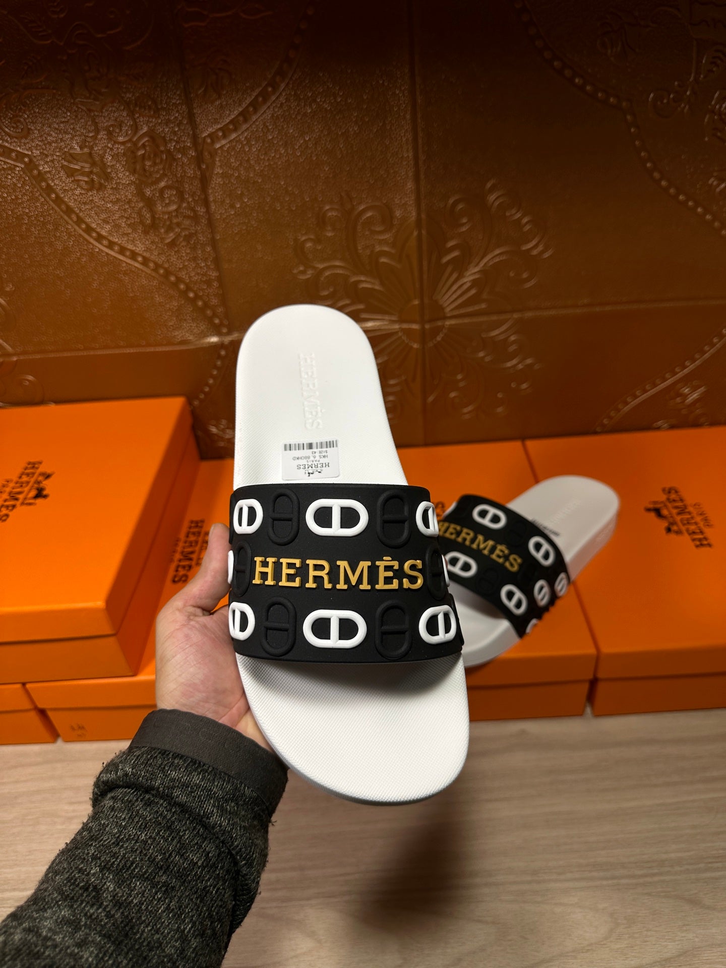 Hermès sandal held up by hand: white footbed with black logo-strap.