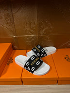 Hermès sandals with white footbeds and black strap with repeating Hermès logos.