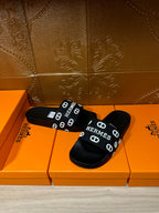 Black slide sandals with wide HERMES logo strap and flat rubber footbed