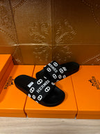 Black slide sandals with HERMES logo strap across the foot, open-toe design