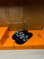 Black slide sandals with wide HERMES logo strap, open toe and textured footbed