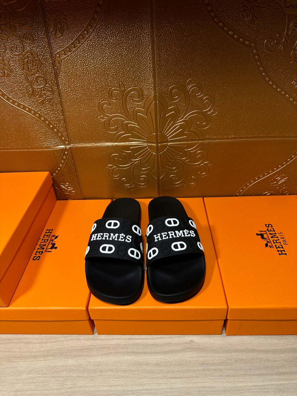 Black slide sandals with wide logo strap, white “HERMES” print and buckle details