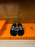 Black slide sandals with wide logo strap, white “HERMES” print and buckle details
