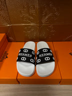 White slide sandal with black Hermes logo strap and repeated monogram pattern