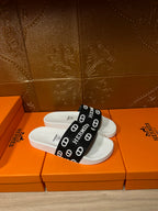White slide sandal with black band strap printed with Hermes letters and icons