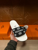 White slide sandal held up with black Hermes logo strap and white footbed