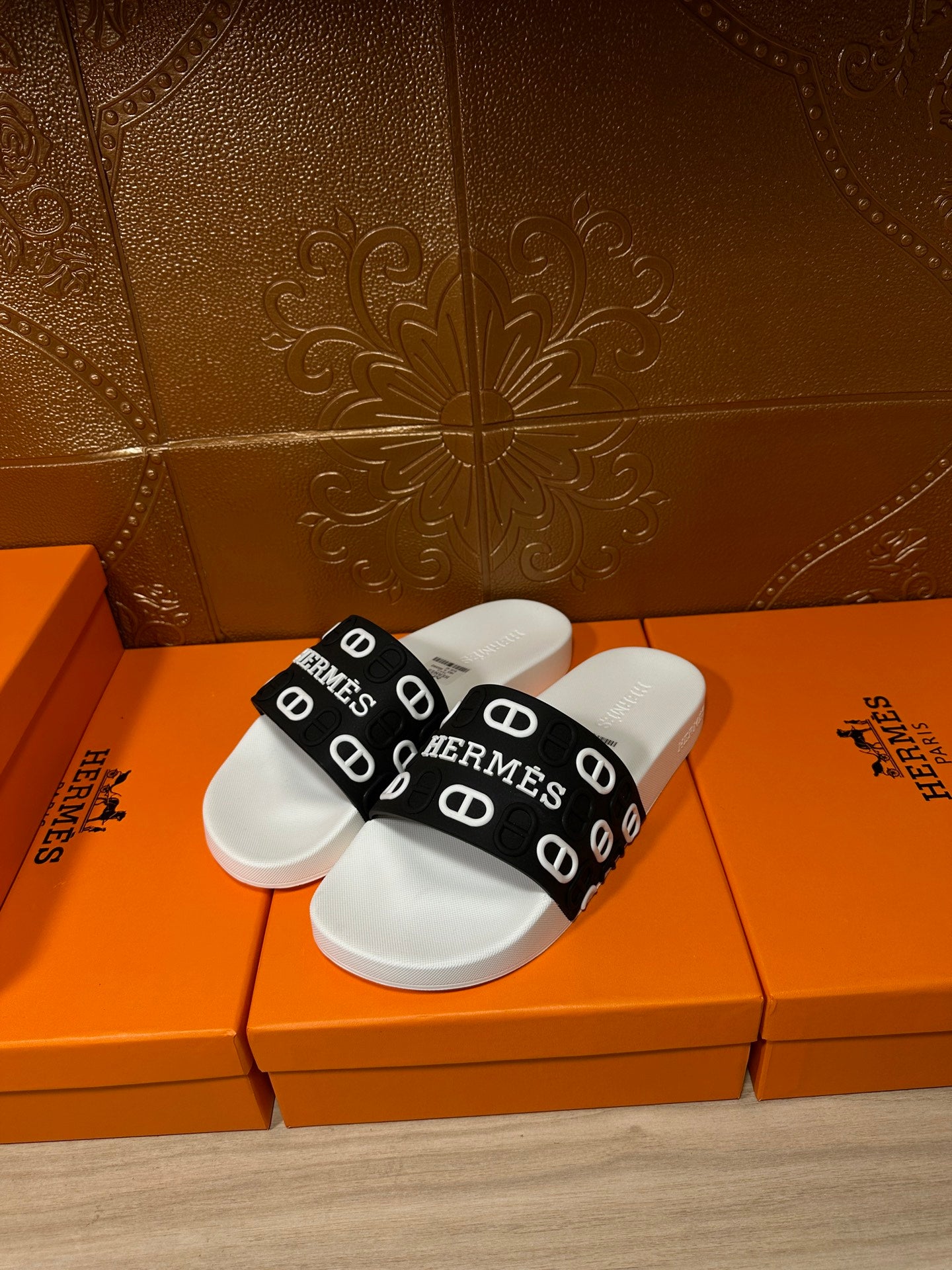 White slide sandal with black strap featuring Hermes logos across the top