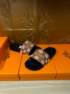 Black slide sandals with brown Hermes logo strap, side view