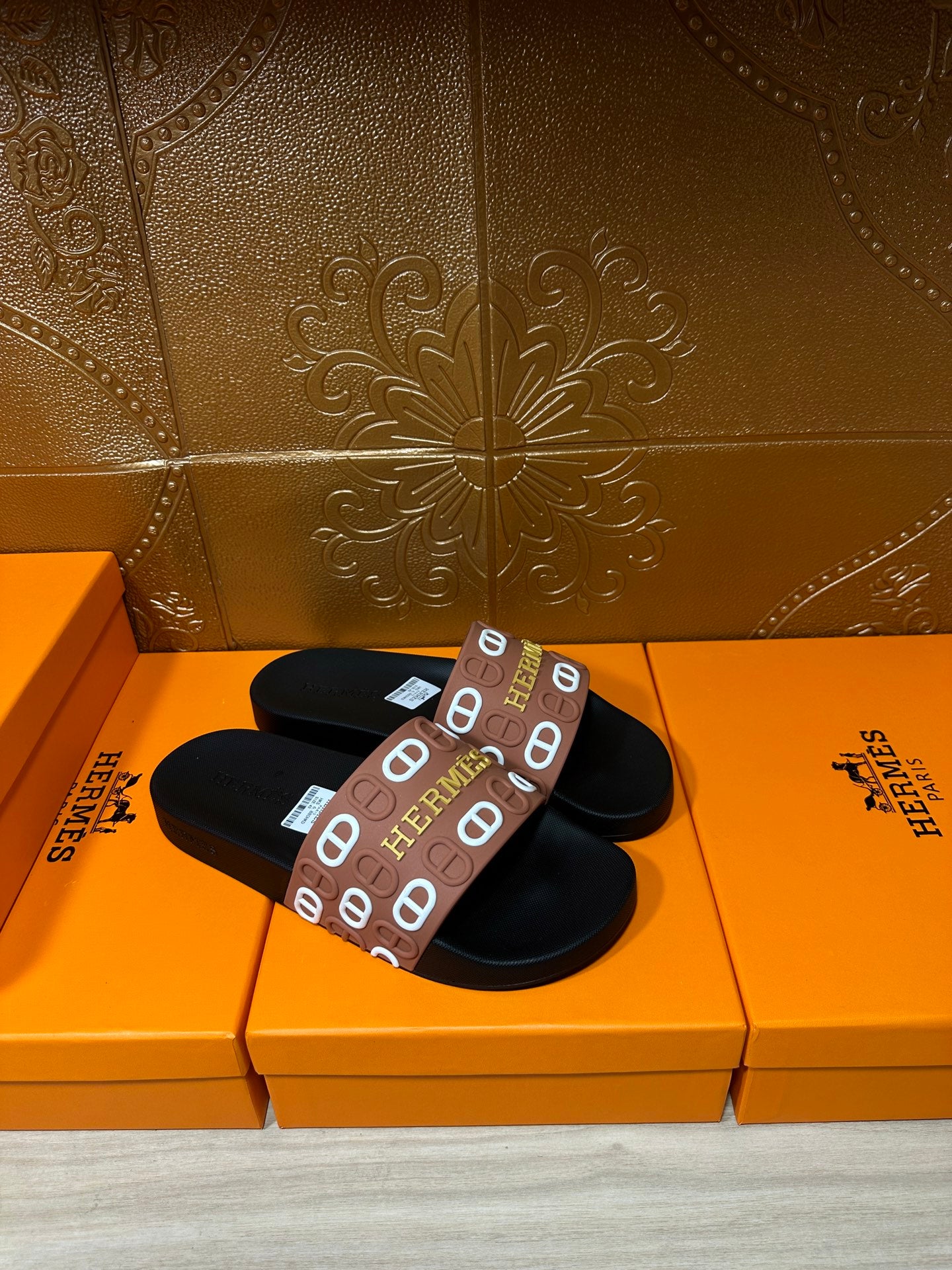 Black slide sandals with brown Hermes logo strap across the top