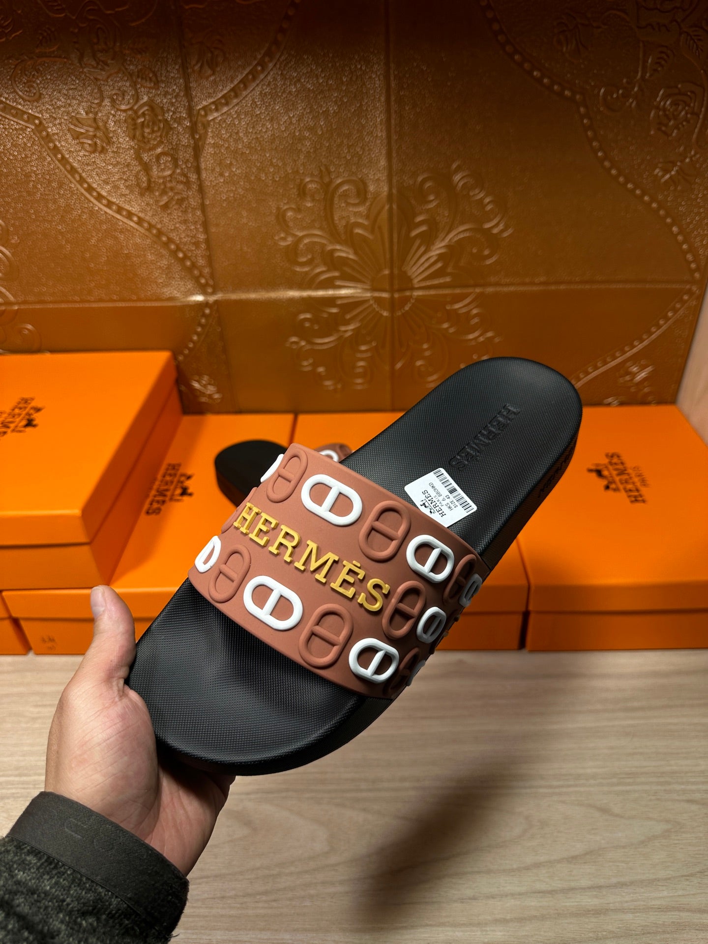 Black slide sandal held in hand, brown Hermes logo strap on top