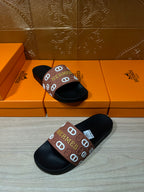 Black slide sandals with brown Hermes logo strap, two sandals spaced