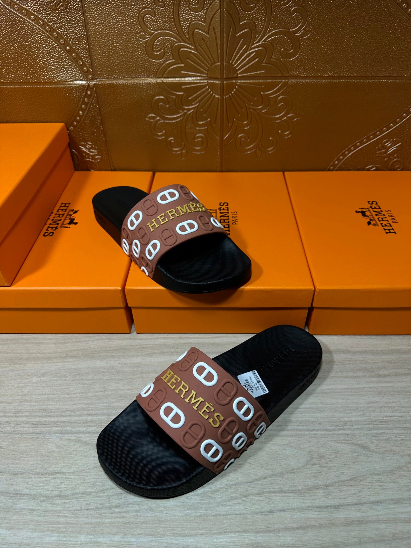 Black slide sandals with brown Hermes logo strap, two sandals spaced