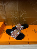Black slide sandals with brown Hermes logo band, angled view