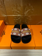 Black slide sandals with brown Hermes logo strap, rounded toe