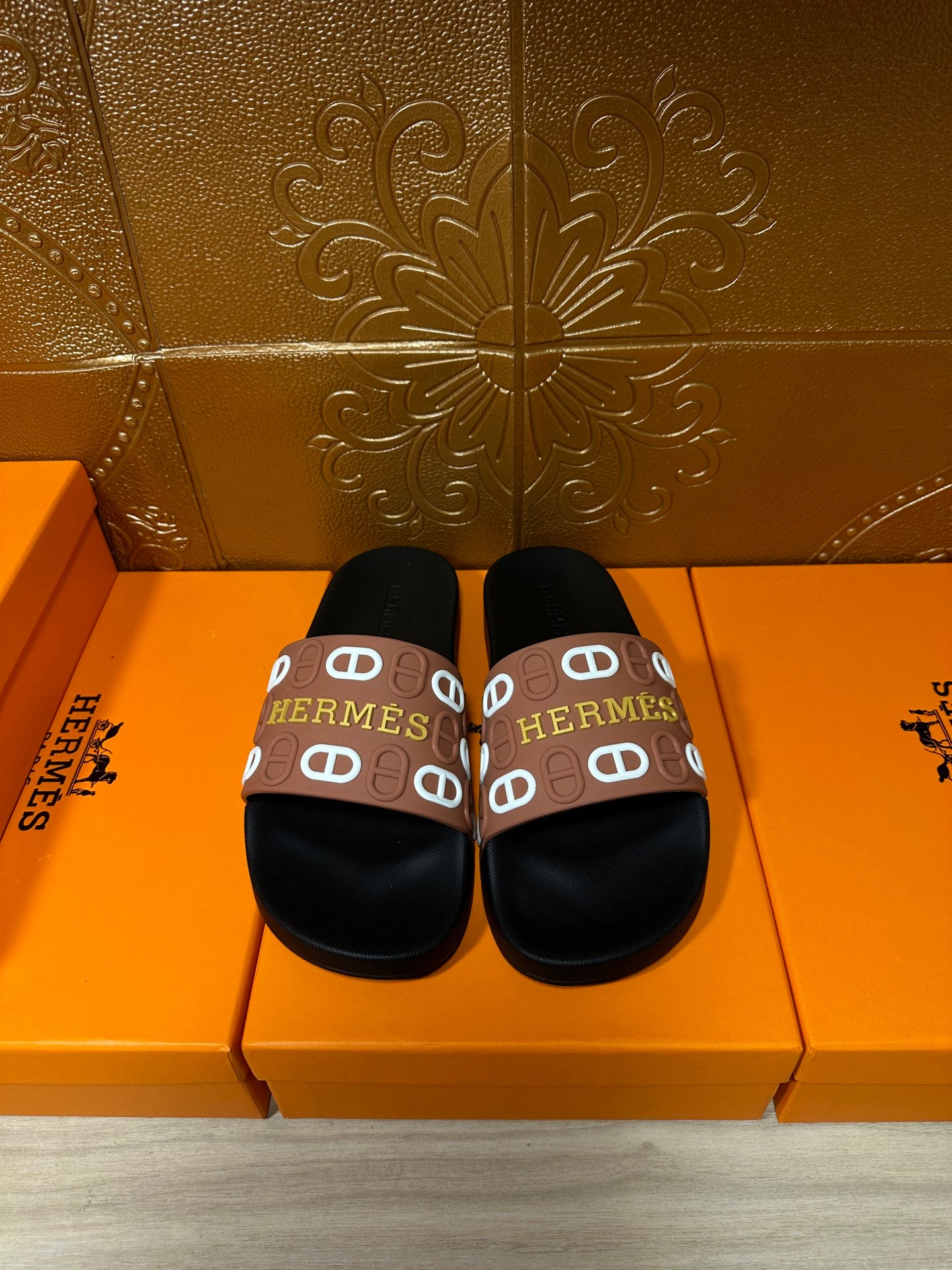 Black slide sandals with brown Hermes logo strap, rounded toe